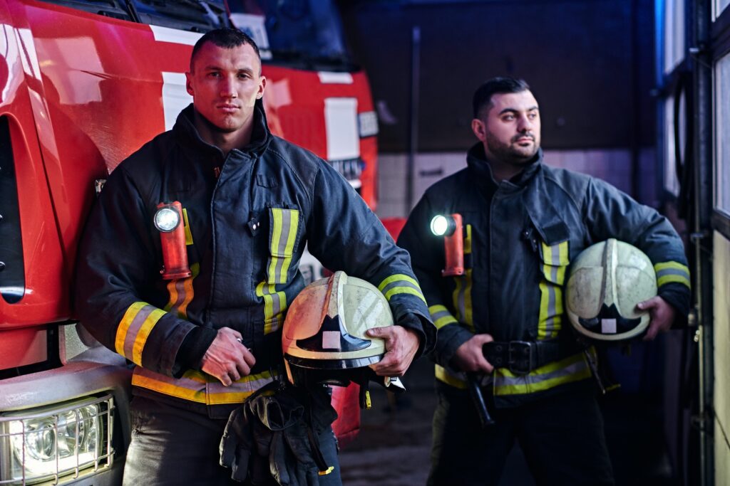 two-firemen-standing-near-the-fire-truck-at-night-in-a-fire-depot-1.jpg